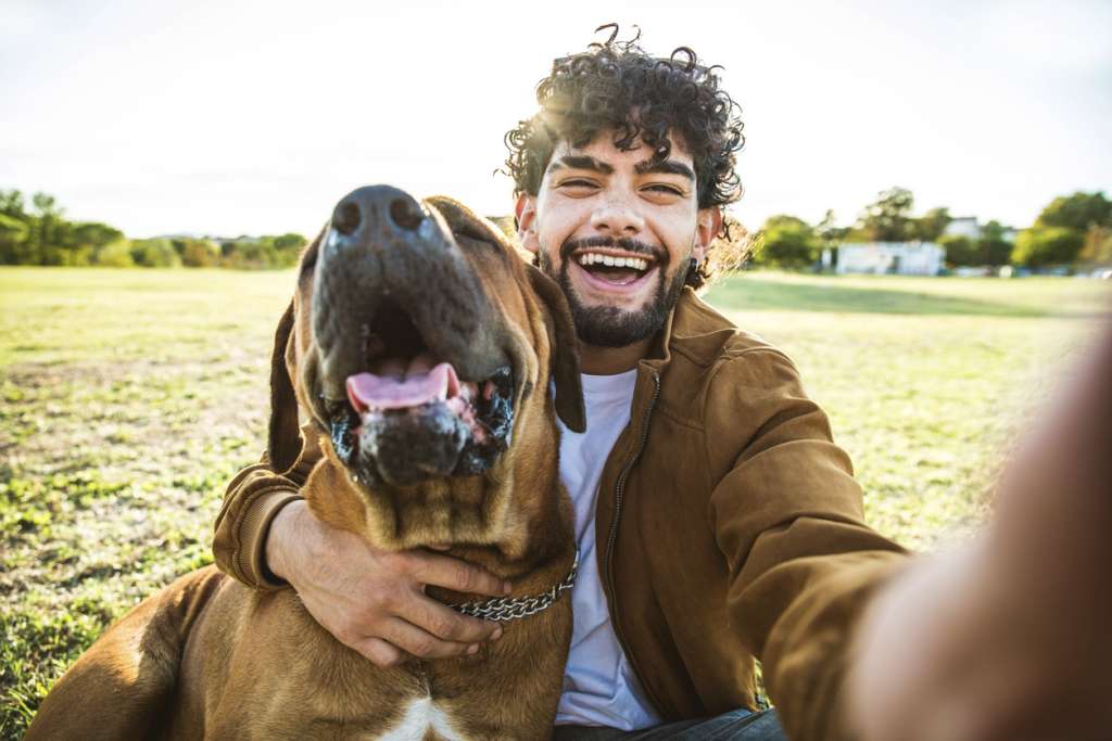 Happy man taking selfie with his dog in a park 